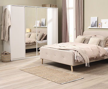 Hvidt garderobeskab med spejl og beige seng i lyst soveværelse