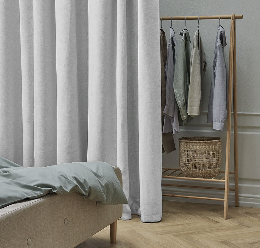 Beige gardin foran tøjstativ adskiller et soveområde fra en garderobe