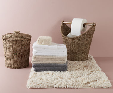 Råhvid bademåtte, toiletspand og toiletrulleholder i flet og bomuldshåndklæder