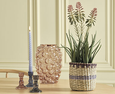 Glaslysestage med stearinlys, glasvase og stribet blomsterpotte med kunstig plante