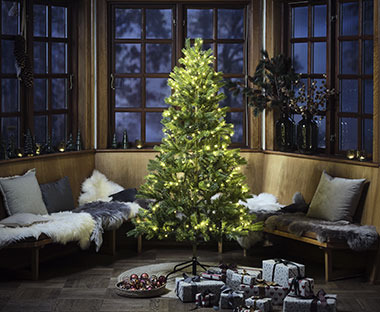 Kunstigt juletræ pyntet med lyskæder og julegaver 
