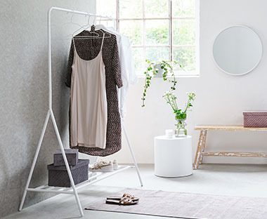 Hvidt tøjstativ med hylde for neden i lyst lokale med rundt spejl på væggen