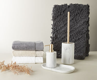 Toiletbørste, sæbepumpe og bakke med marmoreffekt, grå bademåtte og foldede håndklæder