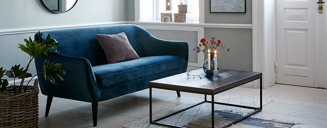 Stue med blå velour sofa og sofabord med tændte stearinlys