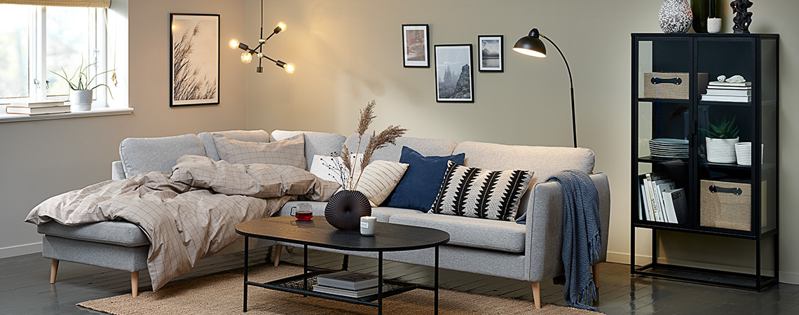 Stue-hygge med grå sofa, dyne, sofapuder, en loftslampe og en sort gulvlampe 