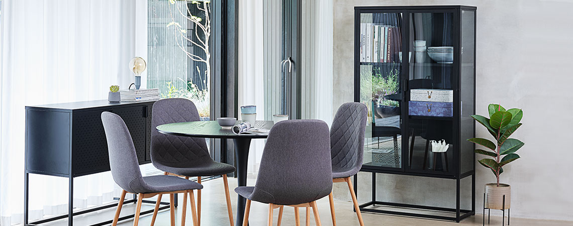 Glasskab i en spisestue med et rundt spisebord og fire grå spisebordsstole