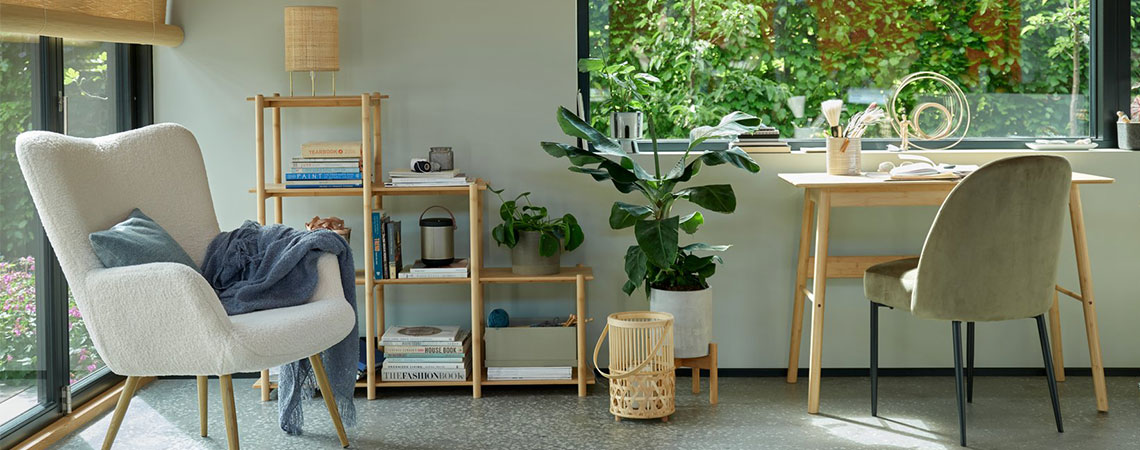 Grå lænestol ved et vindue og en bambus rumdeler i baggrunden. Bambuslanterne på gulvet ved siden af et bambus skrivebord og en grøn spisebordsstol