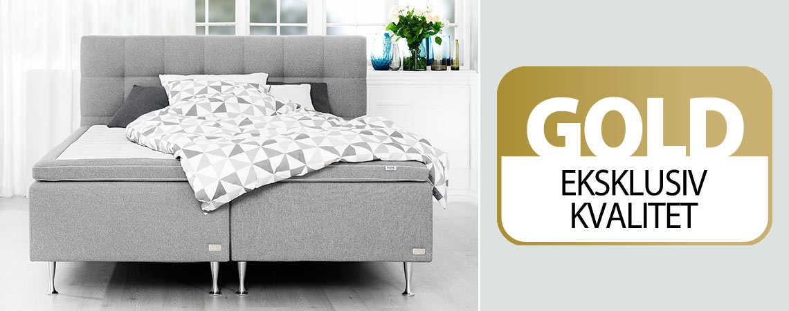 To grå boxmadrasser med topmadras og sengegavl i et soveværelse og GOLD logo