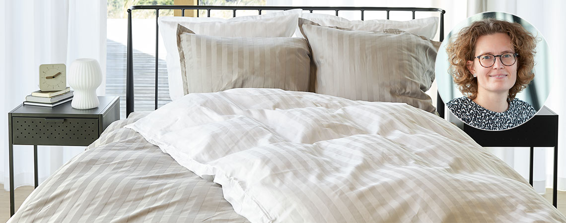 Soveværelse med seng med dyner og puder, betrukket med stribet sengetøj og indsat billede af Berit Christiansen