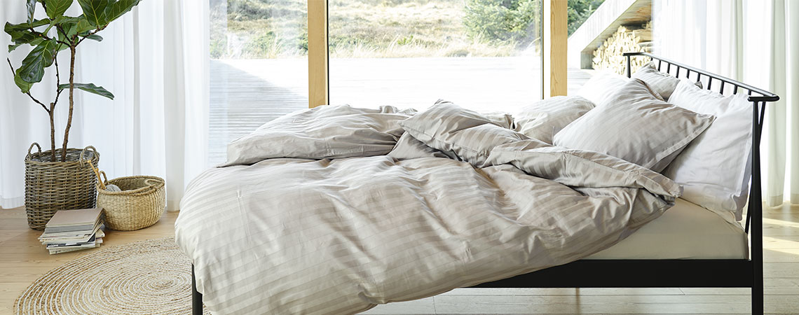 Soveværelse med sort seng i metal samt dyner og puder med stribet sengetøj i lysegrå og hvid 