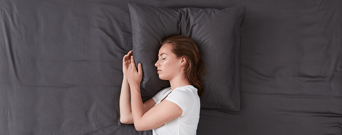 Kvinde sover i seng med mørkegråt sengetøj