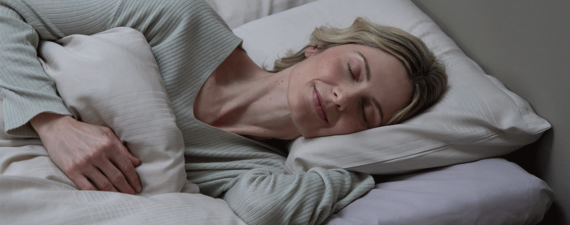 Kvinde sover på siden i seng med hvid pude og dyne