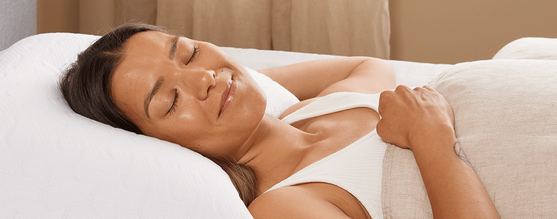 Kvinde sover på ryggen i sengen med pude og dyne