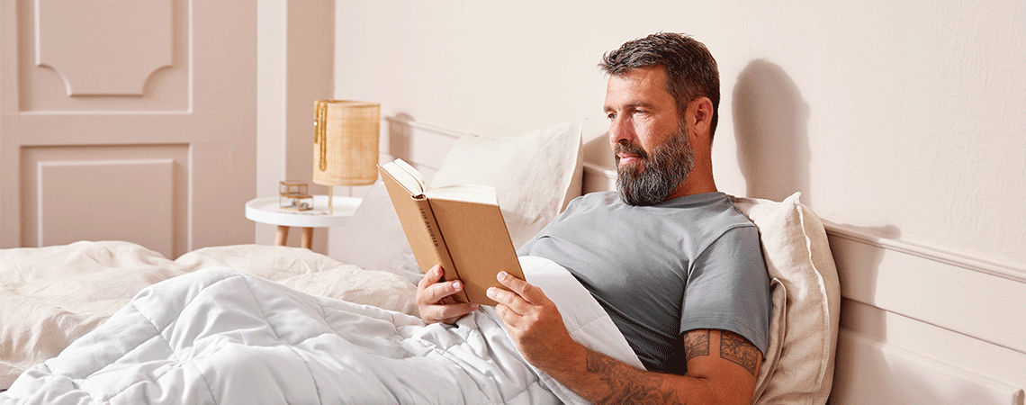 Mand sidder i sengen og læser en bog