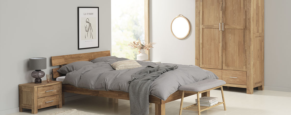 Soveværelse med sengeramme i træ med grå dyner og puder