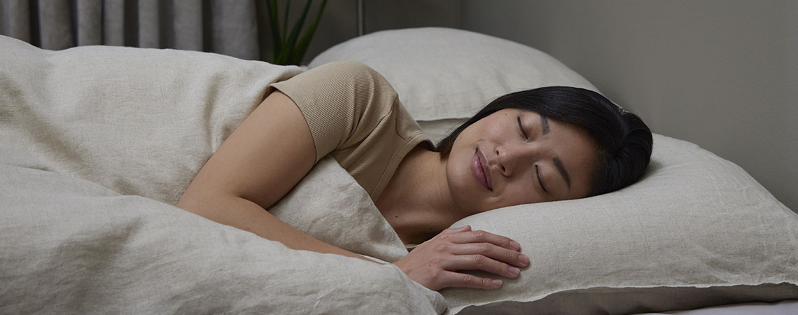 Kvinde sover på siden i sengen med pude og dyne i beige sengetøj