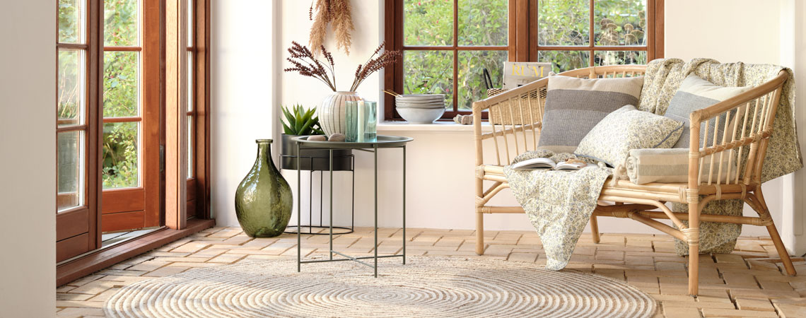 Grøn gulvvase, sort hjørnebord og sofa med vattæppe og blomstret pude i en udestue 