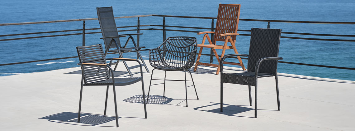 5 forskellige havestole i forskellige materialer på terrasse ved havet