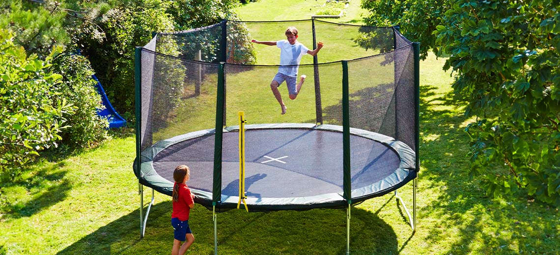 Børn leger på stor trampolin med sikkerhedsnet i have