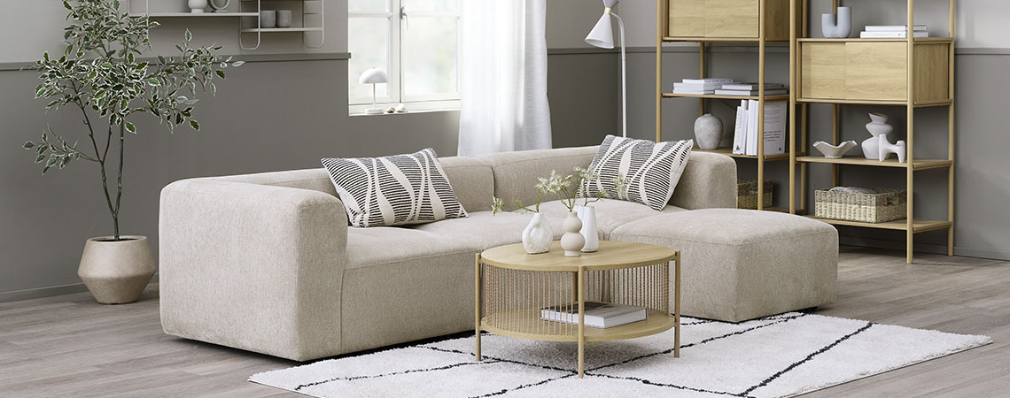 Beige modulsofa i en stue med sofabord, reoler og en plante