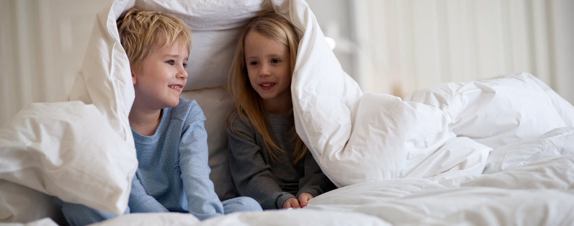 To børn der hygger sig under en dyne i et lyst soveværelse