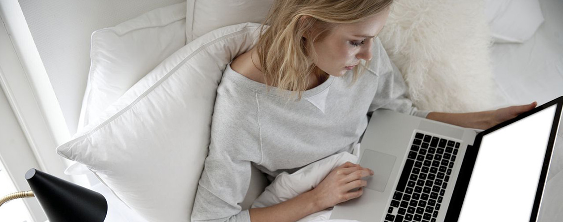 Kvinde der sidder i sengen med en bærbar computer