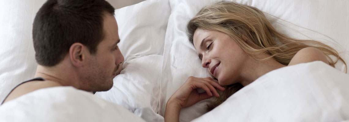 Mand ligger i seng og betragter en smilende kvinde