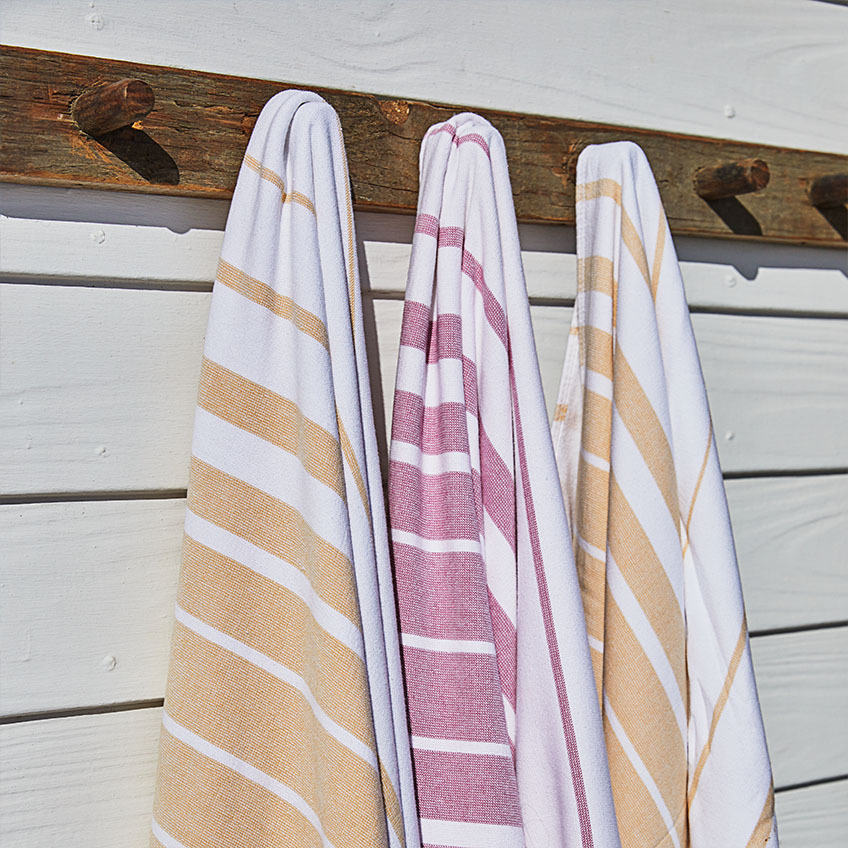 Stribede strandhåndklæder i hvid, orange og pink hængende på trævæg