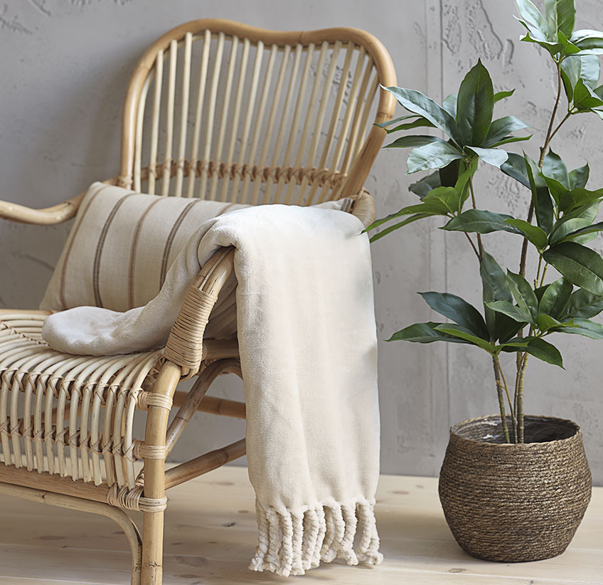 Beige plaid på loungestol i rattan og kunstig plante i planteskjuler