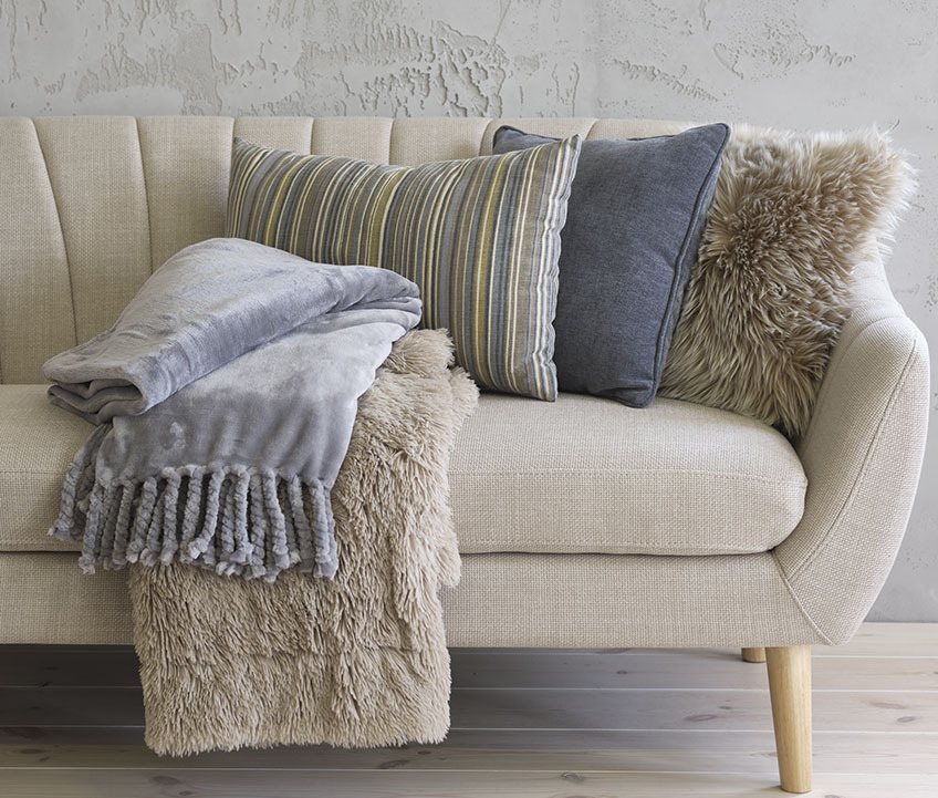 EGEDAL sofa med BONDEROSE fleecetæppe i blå, MYRFIOL plaid i imiteret pels, KORALLROT stribet pyntepude, HORNFIOL blå pyntepude og TAKS pyntepude i imiteret pels Sofa med fleecetæppe, stribede og blå pyntepuder samt imiteret pels pyntepude