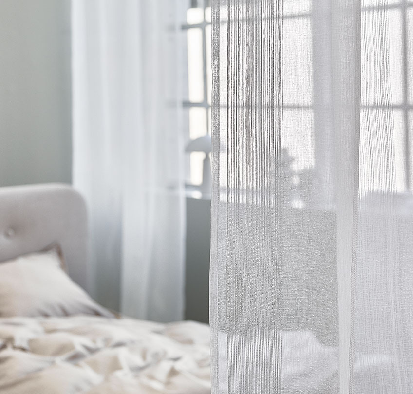 Hvide gardiner der adskiller et soveværelse fra en stor stue 