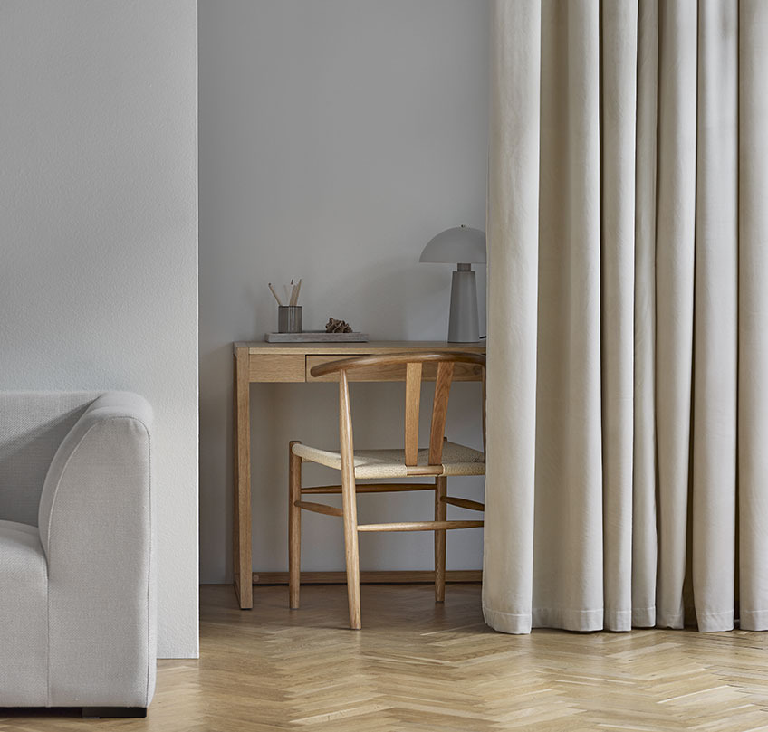 Beige gardiner adskiller et hjemmekontor med skrivebord og stol fra en stue