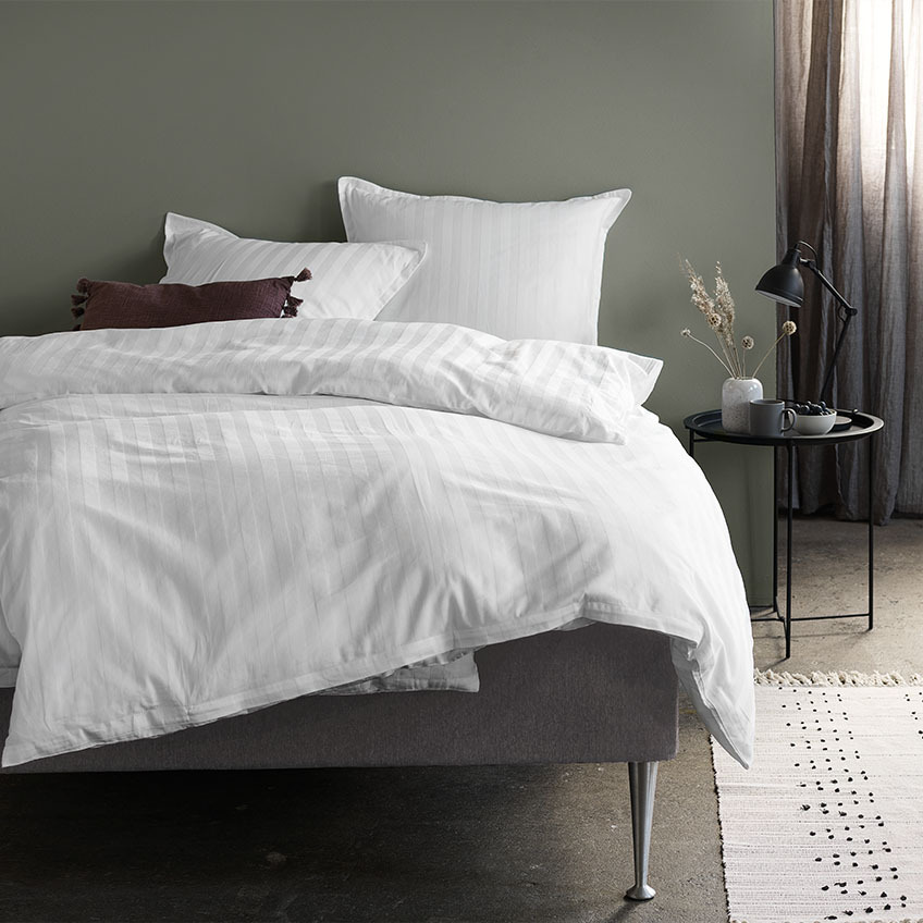 Seng med hvidt sengetøj I soveværelse med natbord og bordlampe