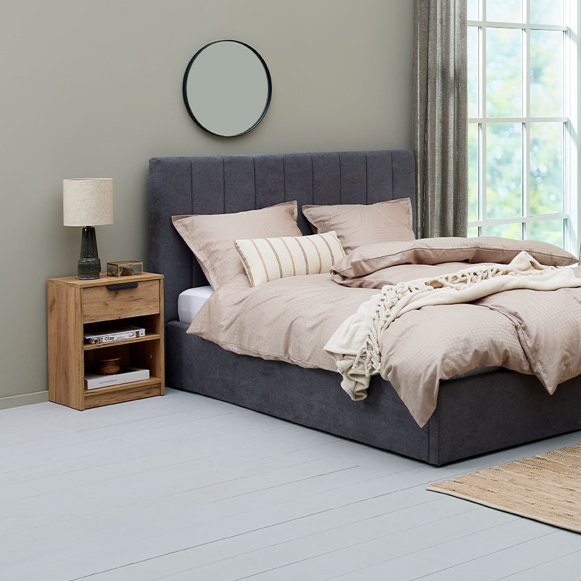 Soveværelse med grå seng, beige sengetøj og sengebord i egetræslook