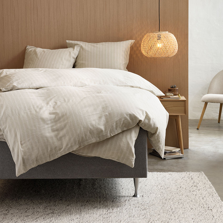Bomuldsflonel sengelinned i en varm beige farve med stribet design på seng i soveværelse