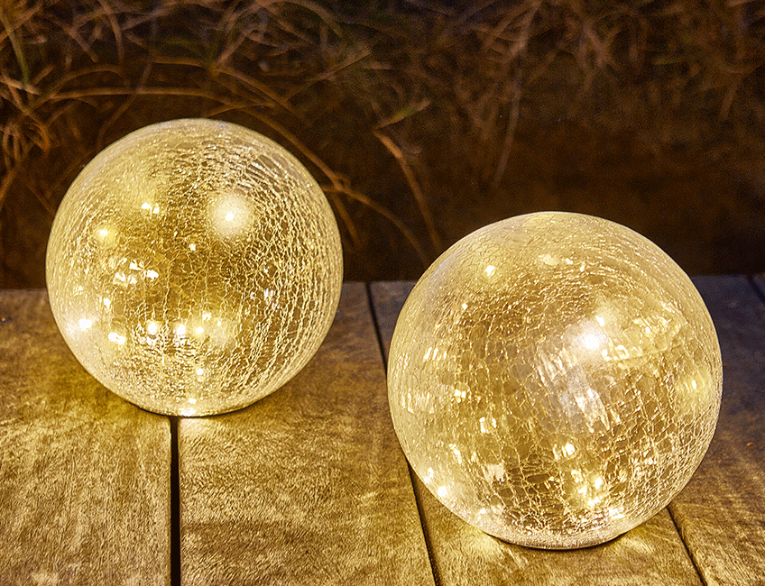 To runde solcellelamper på en træterrasse, der lyser op i mørket