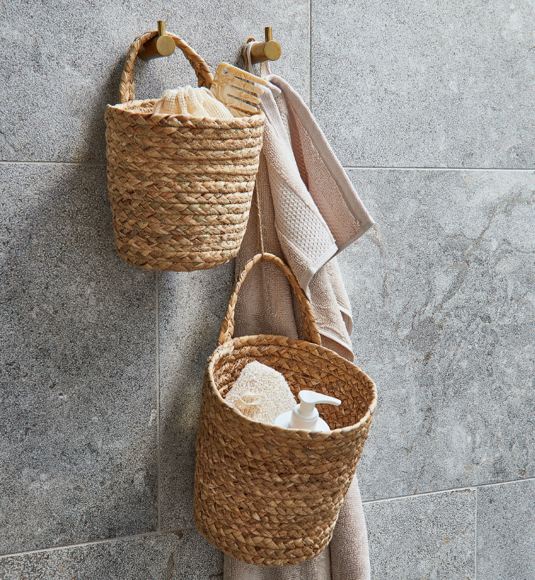 Kurve INGVER hænger på badeværelsets stenfliser ved siden af et badehåndklæde og bruges til opbevaring af bl.a. shampoo og hårbørste
