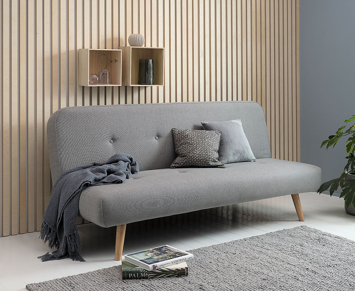 Light grey sofa bed with a throw, small cushions, and some books