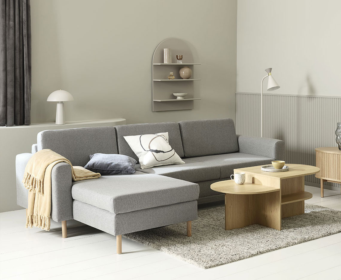 Grey chaise lounge sofa in a living room with coffee table, lamps, and home decorations