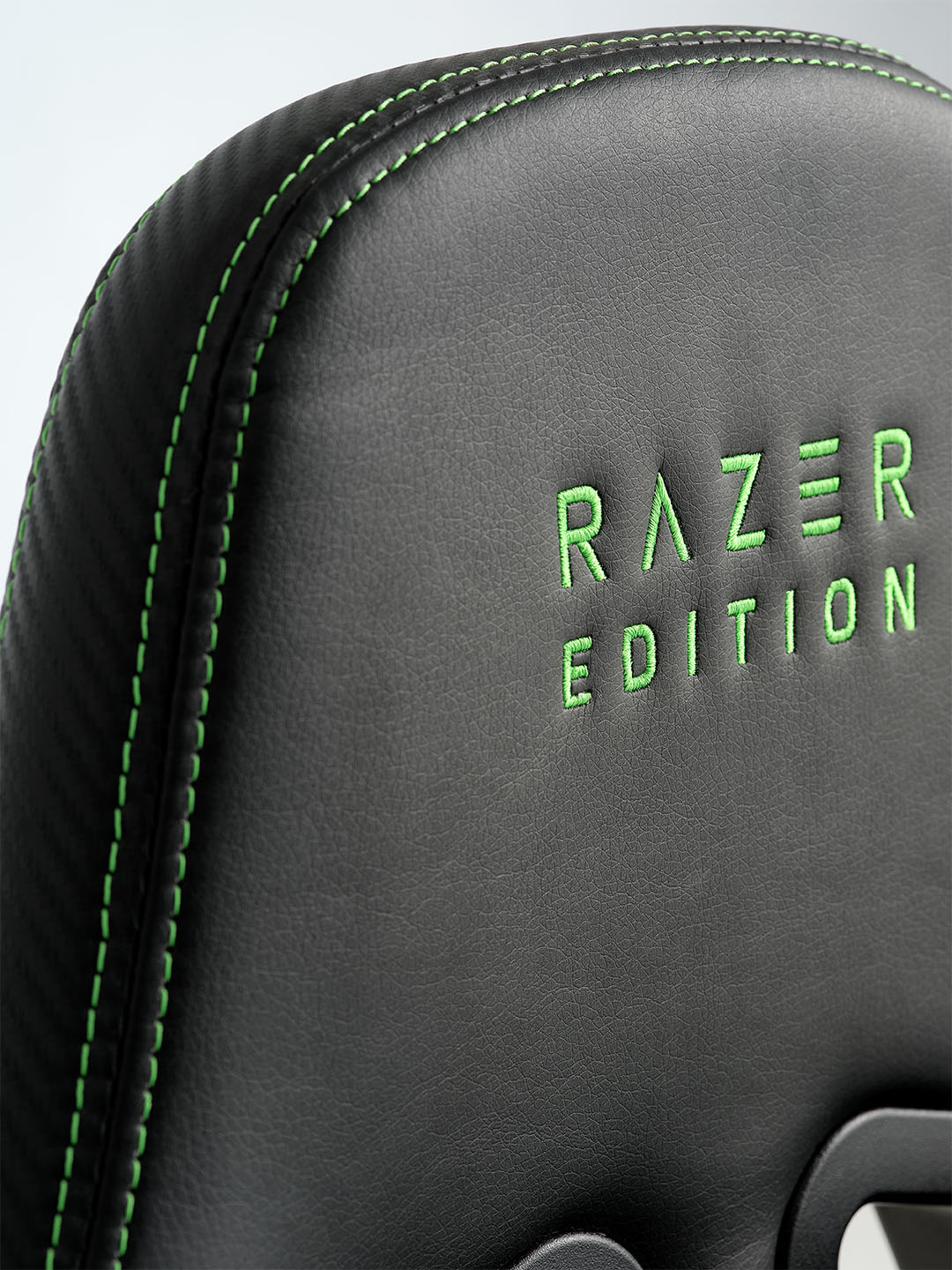 TYPE Z – RAZER EDITION™ BY LEGEND gamerstol Nærbillede af en sort Razer-gamerstol med grønne syninger og "RAZER EDITION" broderet i grønt på ryglænet.