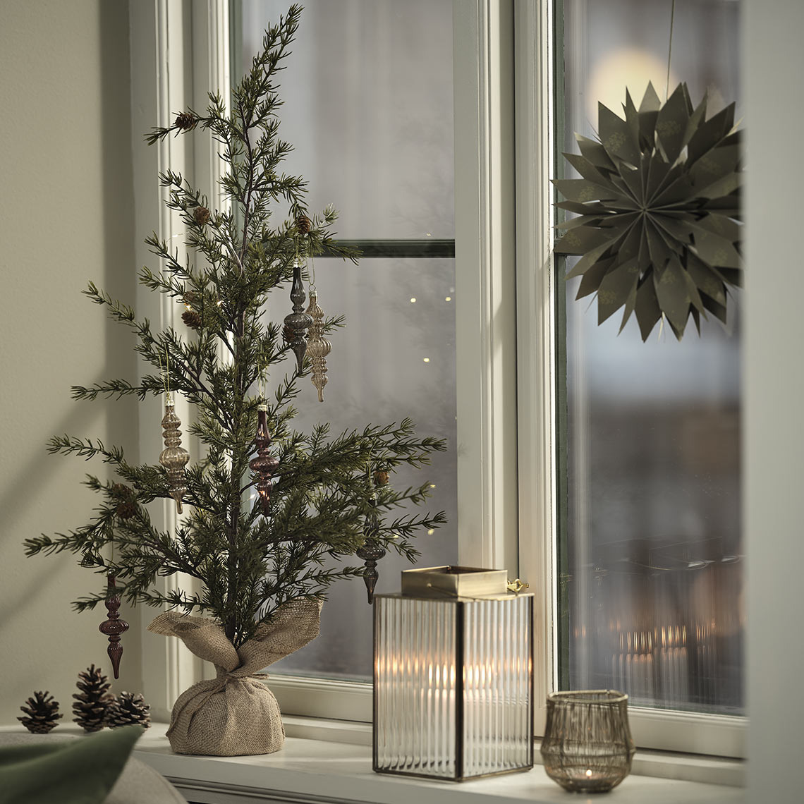 Fyrfadsstage, lanterne og kunstigt juletræ med pynt i vindueskarmen