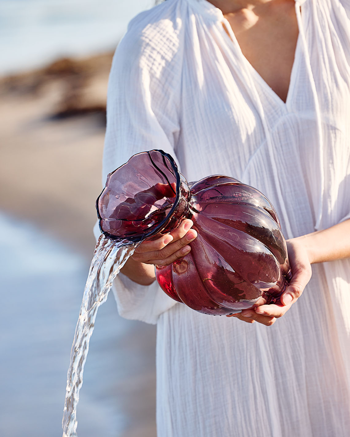 Glasvase i auberginefarve holdes af kvinde på strand