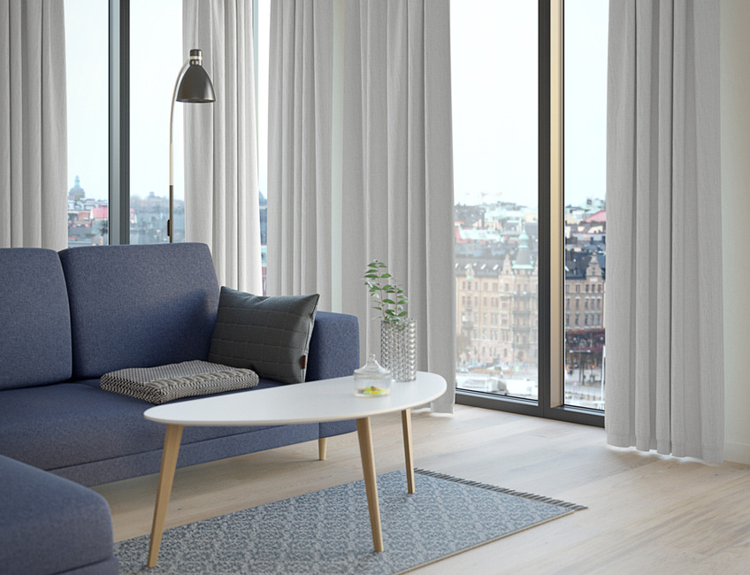 Enkelt indrettet stue med grå sofa og lange lyse gardiner