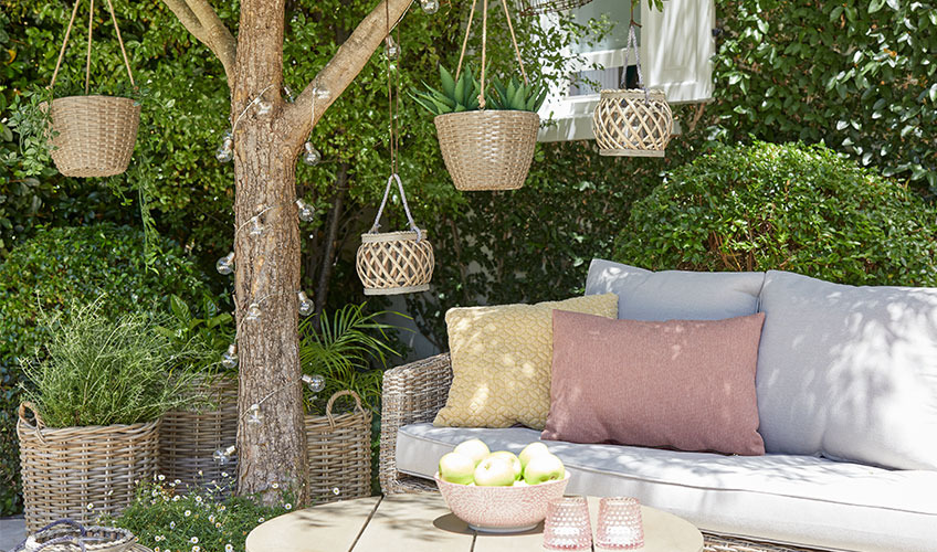 Loungesofa under træ med hængepotter og lanterner i en have