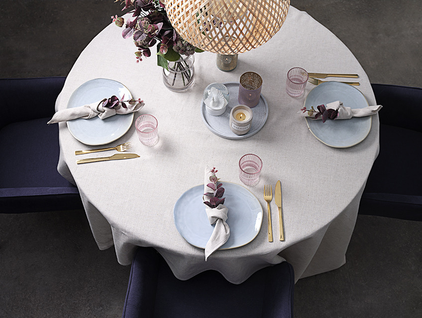 Bord dækket med dug, stofservietter, tallerkener, glas, vase og stearinlys