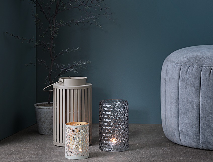FOSS vase, DITLIV lanterne og LENNART holder til fyrfadslys sammen med YNGVAR kunstig plante og DARUP puf Vase, lanterne og holder til fyrfadslys placeret på gulvet i et mørkt hjørne