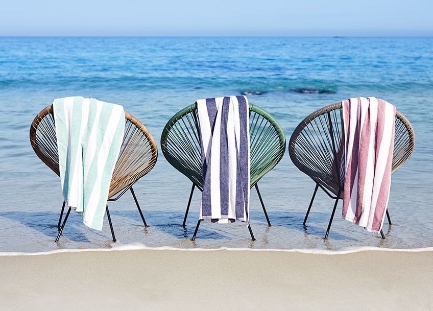 UBBERUP loungestole med MARMA badehåndklæder Loungestole på en strand med strandhåndklæder hængende fra ryggen