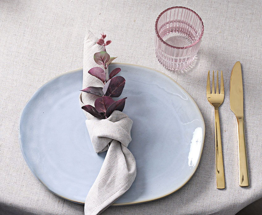 Dekorativ borddækning med tallerken, stofserviet, glas og kniv og gaffel