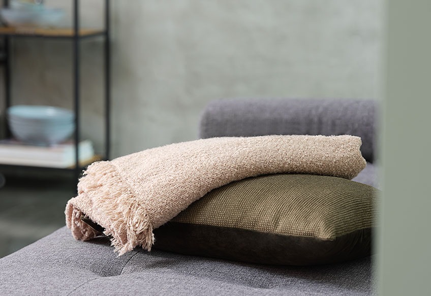 Plaiden ROSE og pyntepuden LILJE En plaid og en pyntepude på en sofa