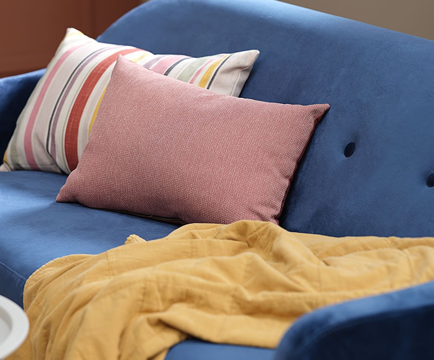 Farverige puder og et vattæppe i en blå sofa